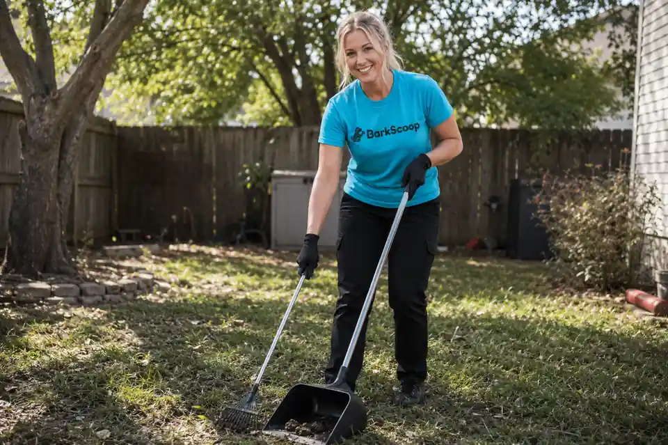 A smiling BarkScoop crew member scooping along the fence line of a shady back yard